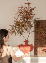 Woman holding a red ribbed vase with dried branches indoors Callista Home