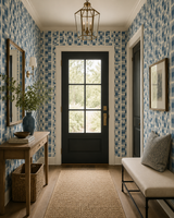 A beautifully styled entryway featuring blue and white mosaic tile wallpaper, a black front door, a wooden console table with a blue vase, a beige bench with a gray pillow, and a natural jute runner on the floor.