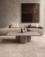 A modern living room scene featuring a textured beige woven sofa, a matching low concrete coffee table, and a large dark brown abstract wall art piece on a textured plaster wall.  Callista Home