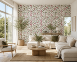 A bright, modern living room featuring a prominent floral wallpaper wall behind a light beige sectional sofa. The wallpaper has a delicate pattern of pink flowers and green leaves on a cream background. Buisson de Roses 58A French floral wallpaper by Antoinette Poisson, inspired by historic domino paper and printed in Brittany, France. Callista Home