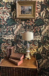 Decorative interior with floral wallpaper, books, and a lamp. Grands Pavots 59A large-scale floral poppy French wallpaper by Antoinette Poisson Callista Home