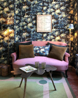 Pink sofa with decorative pillows against a floral wallpapered wall.