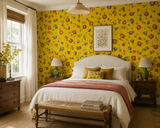 A styled bedroom featuring bright yellow floral wallpaper as the main decor element, with a white bed, matching pillows, wooden nightstands, lamps, a bench at the foot of the bed, and a window with sheer curtains. Callista Home
