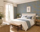 A styled bedroom interior featuring a bed dressed in white bedding with blue pillows and a blue throw, set against patterned blue wallpaper. A light wood bench sits at the foot of the bed, with matching wood nightstands, lamps, a window with sheer curtains, and framed wall art. Callista Home