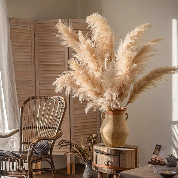 Decorative vase with pampas grass on a wooden barrel in a room with a chair and curtains. Callista Home
