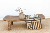 Wooden table with a decorative vase and patterned cloth on a textured surface.