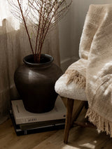 Decorative vase with branches on books next to a chair with a blanket