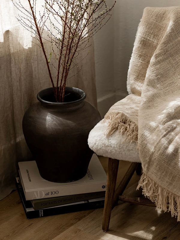 Decorative vase with branches on books next to a chair with a blanket