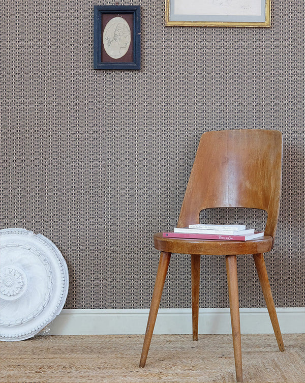 Wooden chair with a pink cushion against a textured wall with framed pictures. Osier Wallpaper Panel 18B by Antoinette Poisson featuring a classic woven basket-inspired French heritage pattern.