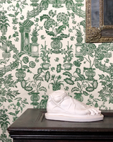 White sculpture on a dark surface with green floral wallpaper in the background