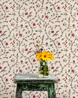 Vase with flowers on a wooden stool against a floral wallpapered wall.