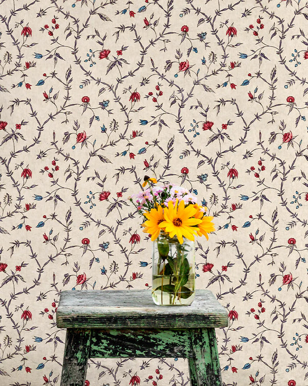 Vase with flowers on a wooden stool against a floral wallpapered wall.