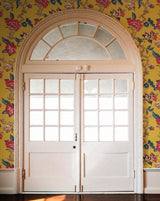 A pair of white double doors with multiple square glass panes and a decorative arched transom window above, set against a bright yellow floral wallpaper.