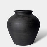 A matte black ceramic vase with a rounded body and a flared rim, photographed on a clean light gray background.
