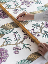 Person measuring floral and bird patterned fabric with a wooden ruler, Colonne 31A architectural French linen fabric by Antoinette Poisson Callista Home