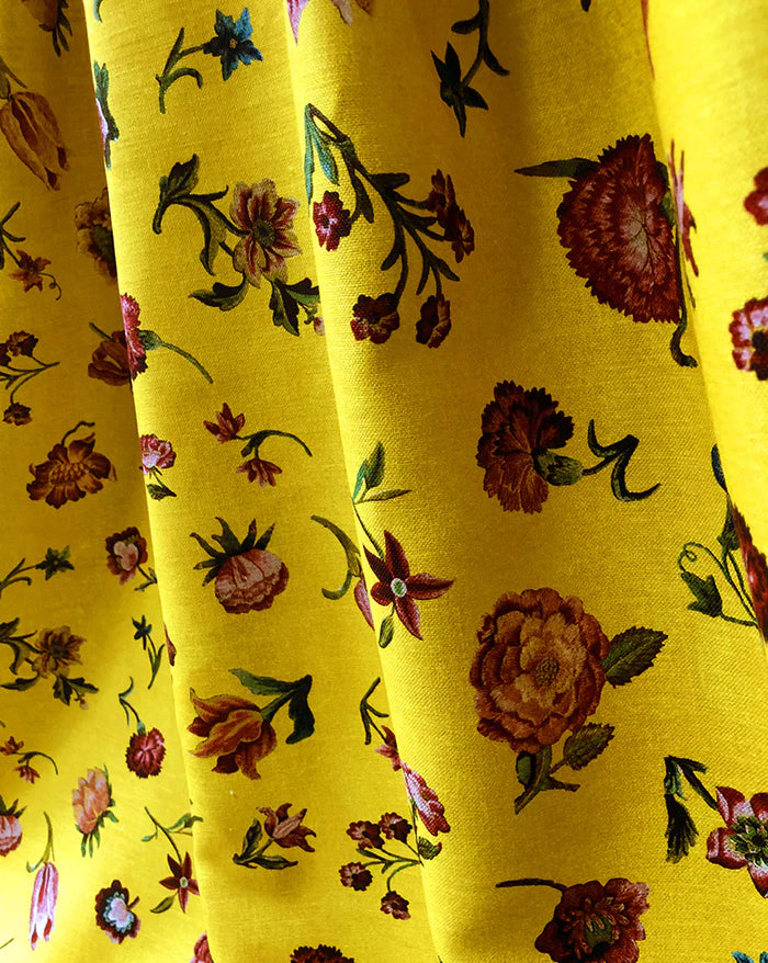 Yellow fabric with a dense floral print featuring red, orange, and pink flowers with green leaves, shown in soft vertical folds. Bien Aimée botanical floral French linen fabric Callista Home