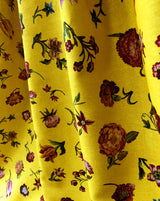 Yellow fabric with a dense floral print featuring red, orange, and pink flowers with green leaves, shown in soft vertical folds. Bien Aimée botanical floral French linen fabric Callista Home