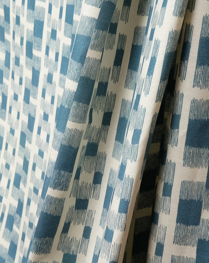 A close-up of draped fabric with an abstract geometric pattern in slate blue and cream. Ikat 14A geometric French linen fabric by Antoinette Poisson Callista Home