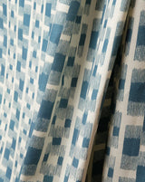 A close-up of draped fabric with an abstract geometric pattern in slate blue and cream. Ikat 14A geometric French linen fabric by Antoinette Poisson Callista Home
