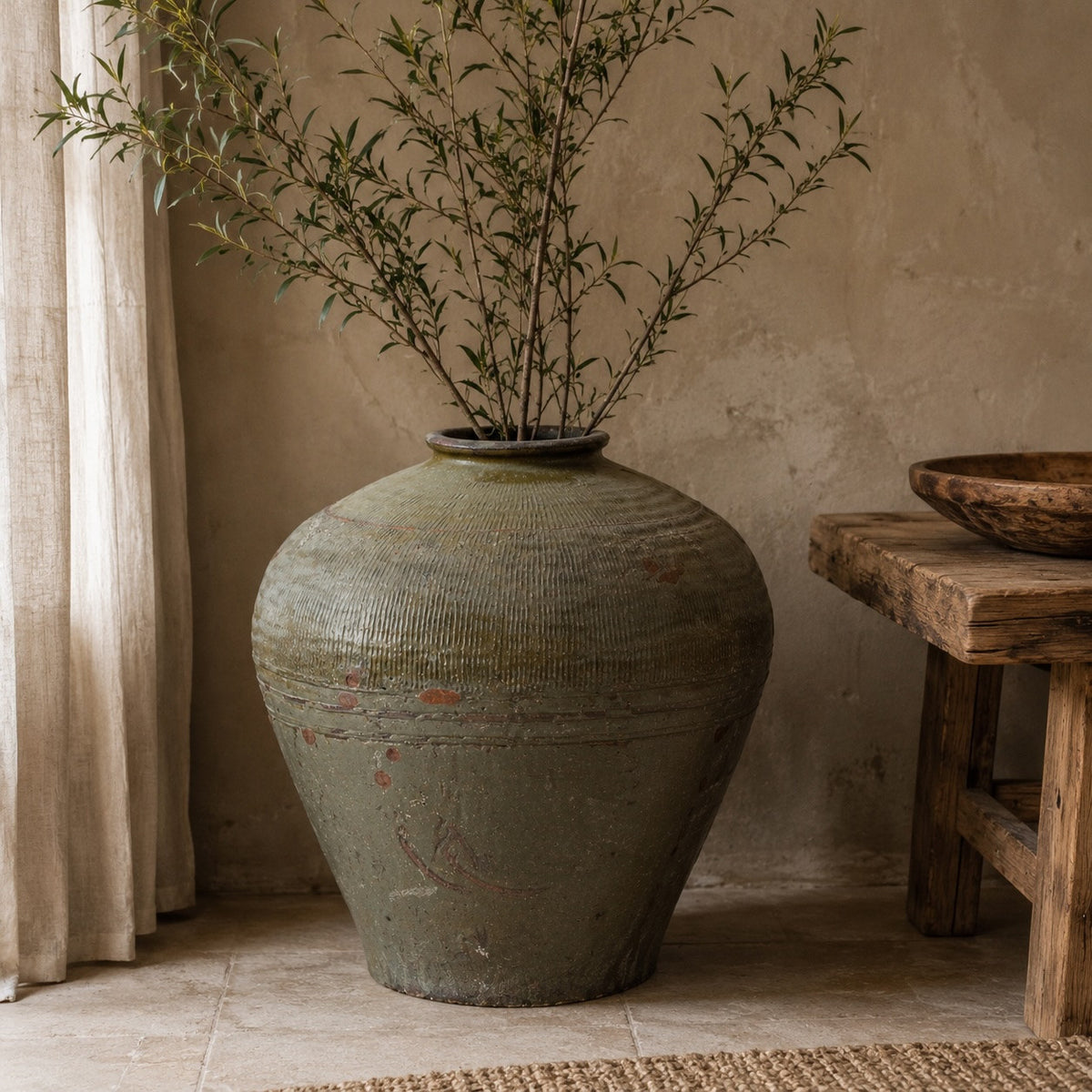 Vintage-style vase with branches on a wooden table against a beige wall.