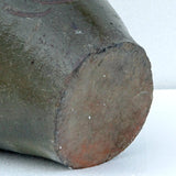 Close-up of the round base of a dark glazed ceramic vessel, showing a brown and reddish-brown unglazed footring against a light gray background.