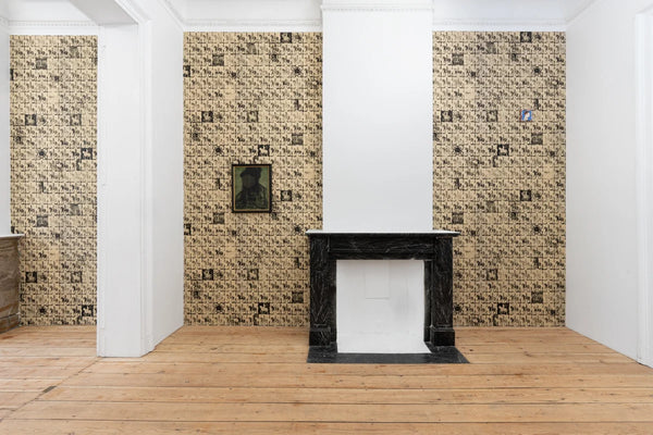 A styled interior room with three patterned wallpaper panels on the walls, a black marble fireplace mantel, light wood floors, and white columns.