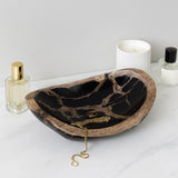 Decorative stone bowl with jewelry on a white surface, next to a candle and perfume bottle. Callista Home