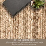 A close-up of a woven natural fiber rug or mat with a dark rectangular book and a small potted succulent placed on top. Text at the bottom reads, 'JUTE IS A NATURAL FIBER' with smaller explanatory text about subtle color variations and lighting. Callista Home