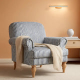 A striped armchair with blue and white vertical stripes, featuring turned wooden legs and a cream throw blanket draped over the arm, set in a warm peach-colored room next to a side table. Callista Home