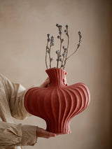Person holding a textured red vase with dried branches against a beige background Callista Home