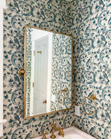 Bathroom with decorative wallpaper, mirror, and gold fixtures. Oiseaux & Feuillages 24A French wallpaper by Antoinette Poisson featuring an elegant bird and foliage pattern inspired by historic domino papers. Callista Home