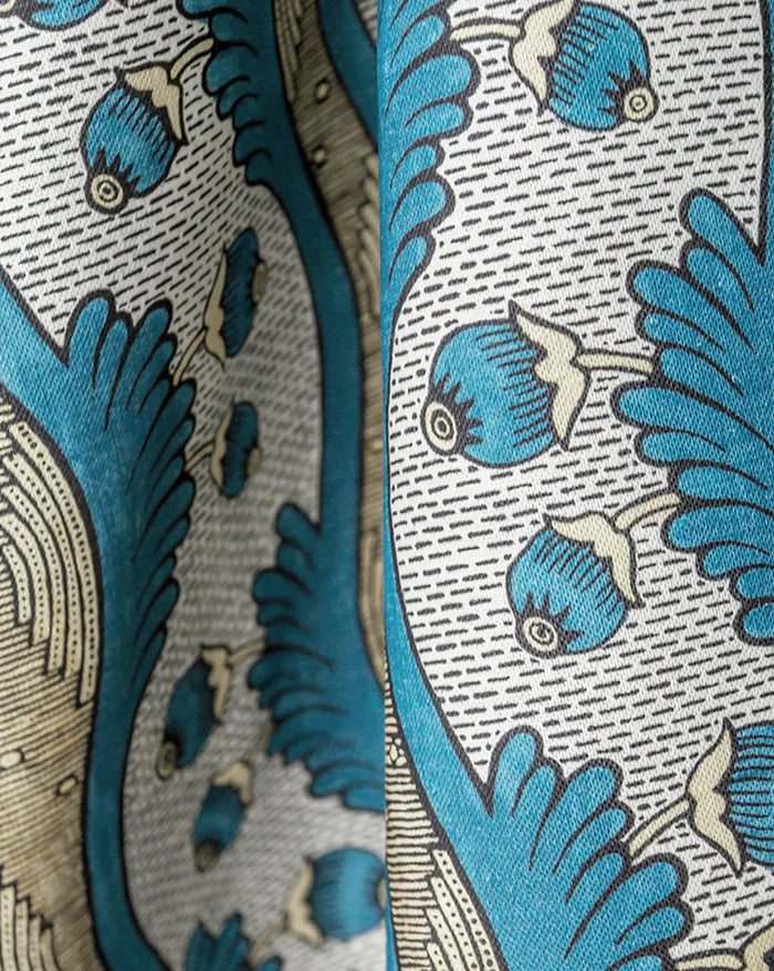 Close-up of a patterned fabric with blue stylized floral or leaf motifs, beige outlines, and a white background with fine gray herringbone lines. Callista Home, Grenades 2A botanical pomegranate French linen fabric