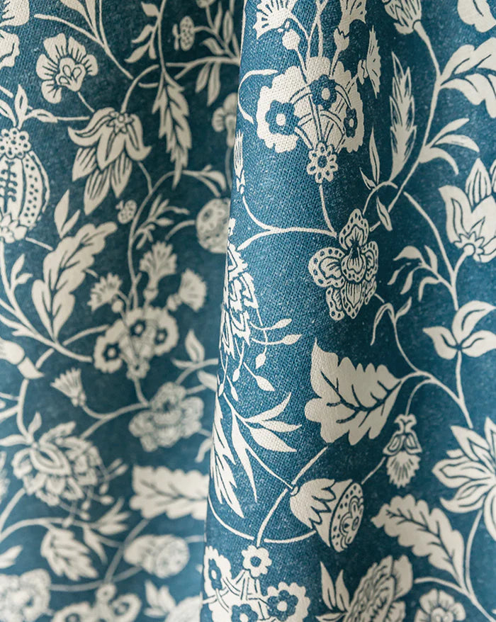 A close-up of draped fabric with an allover floral and botanical print in off-white on a deep teal-blue background. Callista Home
