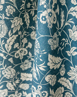 A close-up of draped fabric with an allover floral and botanical print in off-white on a deep teal-blue background. Callista Home