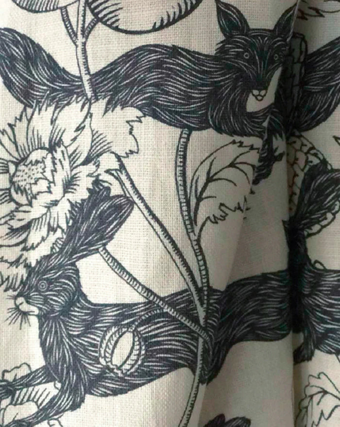 A close-up of a fabric or wallpaper pattern featuring black line-art illustrations of foxes and wildflowers on an off-white background. Callista Home