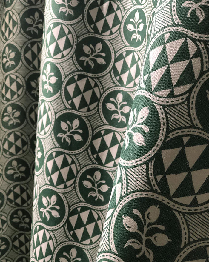 A close-up of patterned fabric with a repeating circular medallion design in dark green, cream, and gray, shown with soft folds. Olives 55A botanical French linen fabric by Antoinette Poisson Callista Home