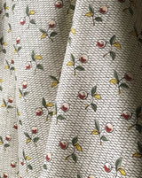 A close-up of a draped fabric with a repeating pattern of red cherries with green leaves and yellow accents on a cream background with fine black dotted lines. Baies 56A botanical berry French linen fabric Callista Home