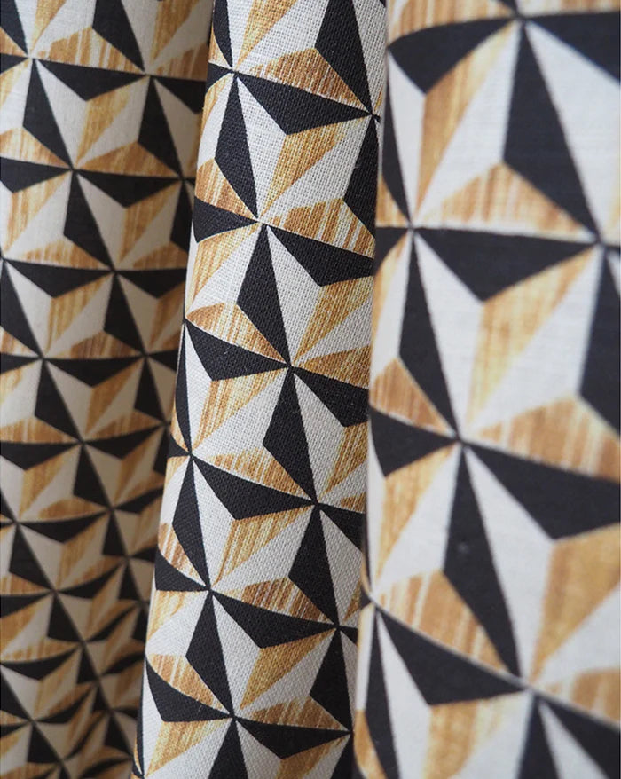 Close-up of patterned fabric with a repeating geometric triangle design in black, white, and warm tan woodgrain-like tones. Callista Home