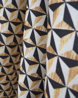 Close-up of patterned fabric with a repeating geometric triangle design in black, white, and warm tan woodgrain-like tones. Callista Home